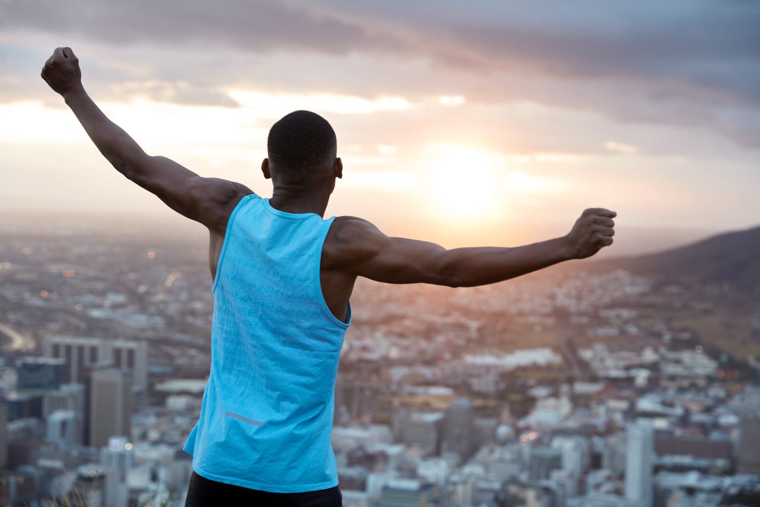 carefree-independent-man-with-dark-skin-stands-back-stretches-hands-as-holding-world-feels-freedom-wears-blue-casual-vest-enjoys-panoramic-view-with-sunrise-recreation-concept-1